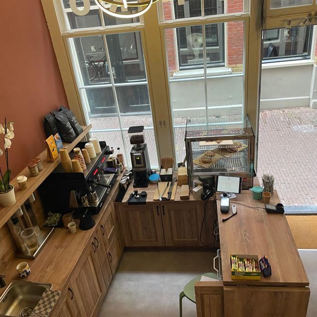 Kijkje van bovenaf op de koffiebar, de vitrine met gebak en de winkelingang van Bakaliko Amsterdam