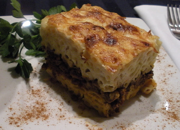 Slice of pastitsio with pasta, a minced meat layer and béchamel, parsley on the side