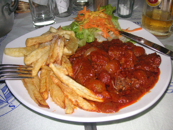 Plate of stifado stew in tomato sauce with fries