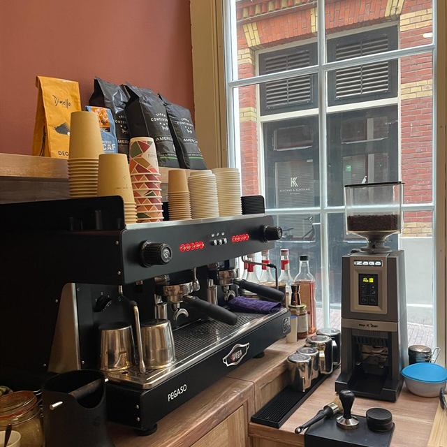 Koffiehoek met espressomachine en koffiemolen bij het raam van Bakaliko Amsterdam